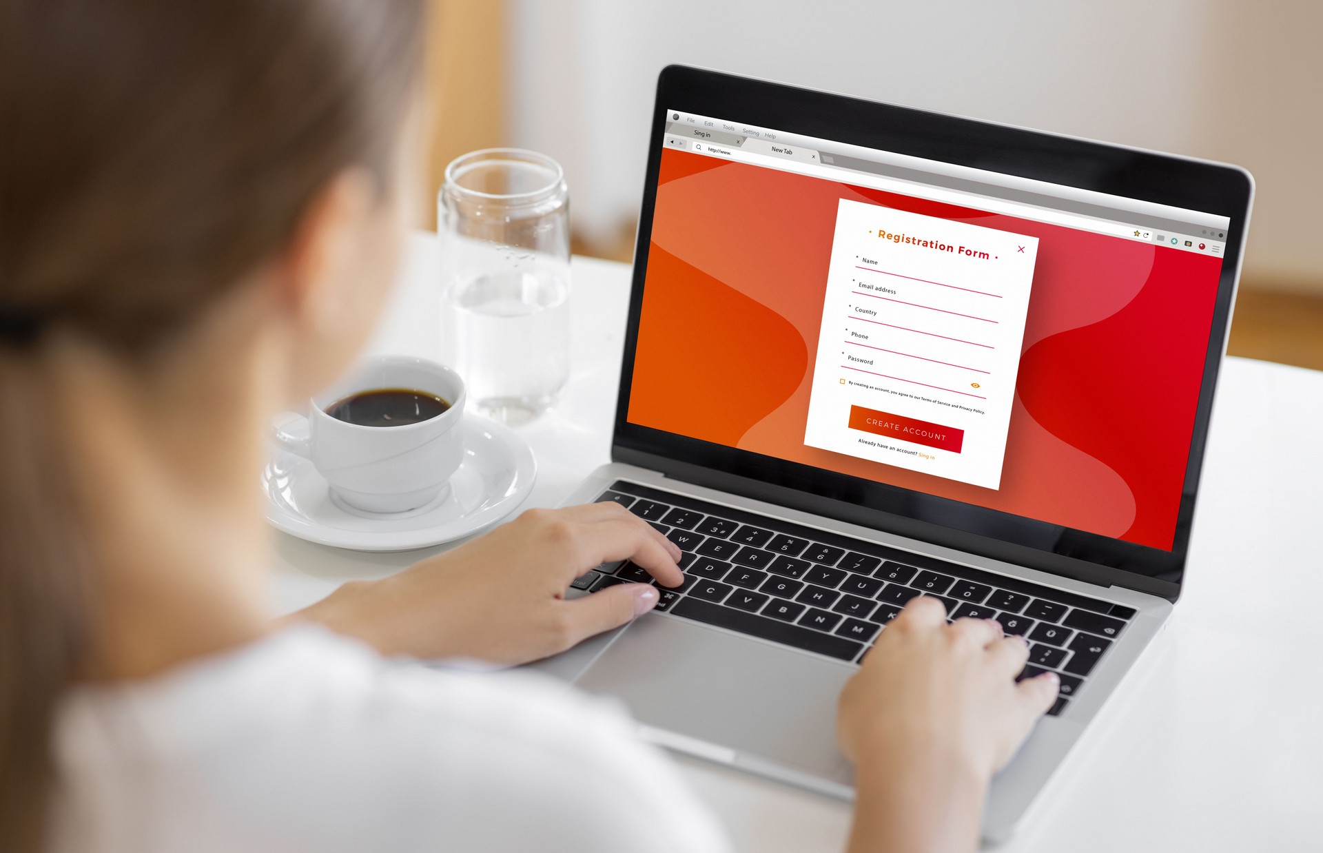 Woman Registering Online Account on Laptop with Coffee and Water on Desk